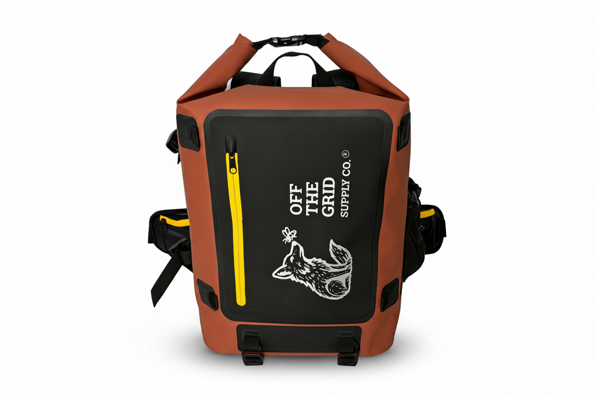A waterproof dry bag backpack in rust orange and black, featuring a yellow zipper, a white graphic of a fox wearing sunglasses, and the text 'OFF THE GRID SUPPLY CO.' on the front, shown against a plain white background.